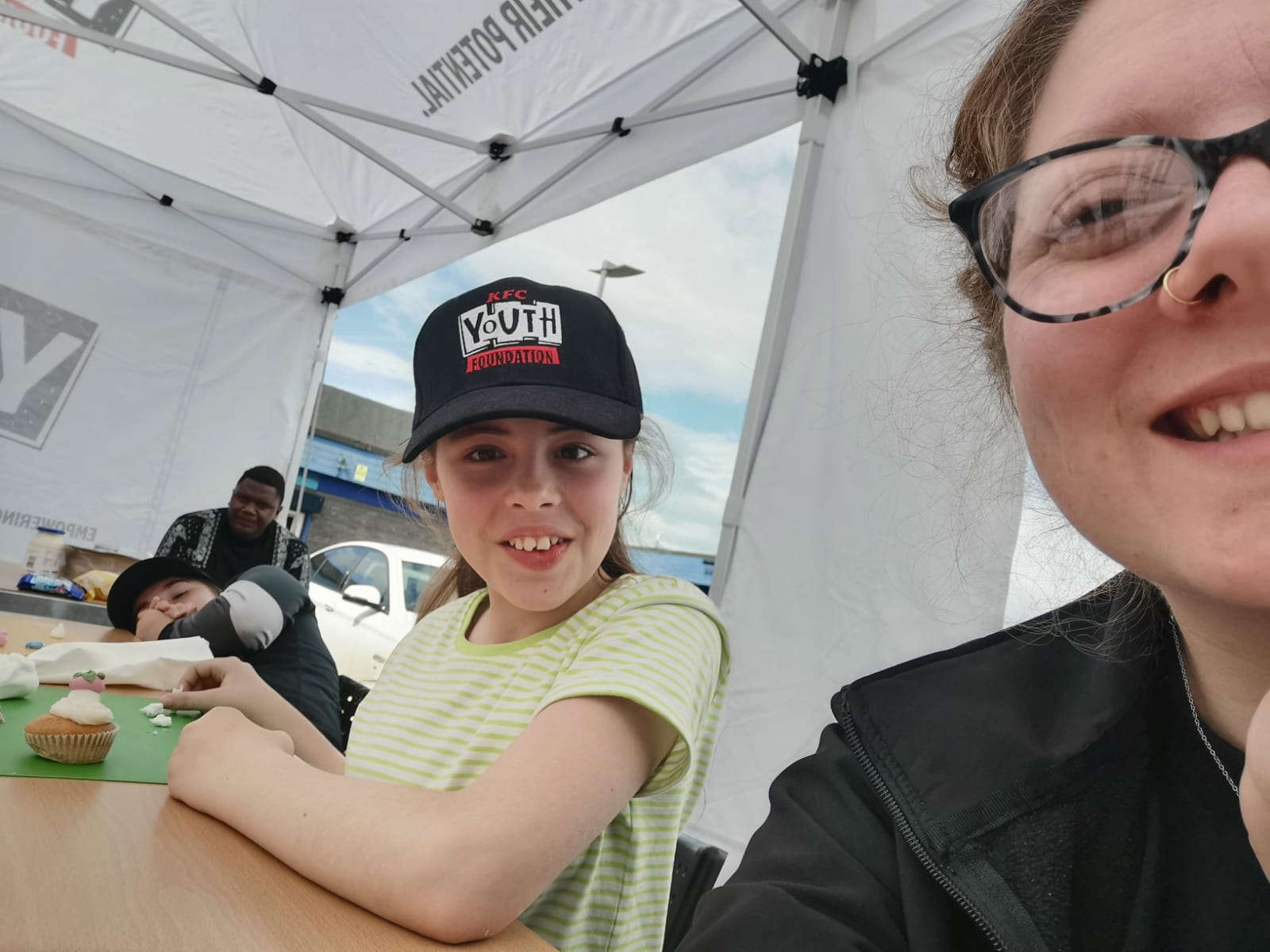 A very smiley young lady decorating a cupcake with a youth worker