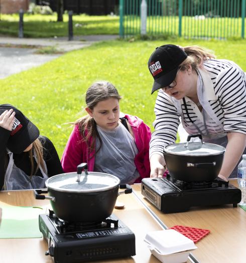 Young people with a youth worker turning on the portable hot plate and pot to cook